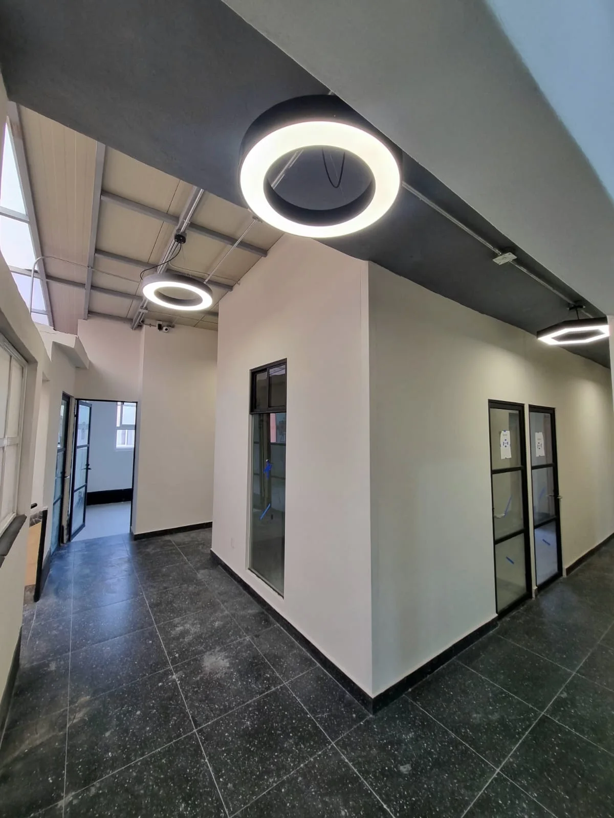 Pasillo de consultorios con luminarias circulares y piso oscuro